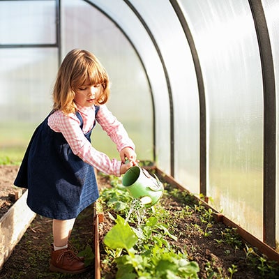 a small girl watering plants in a greenhouse