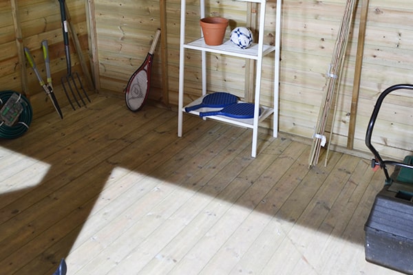 wooden shed floor close up with several tools, shelves and mower visible
