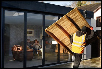 a shed courier carrying a wooden panel into a garden