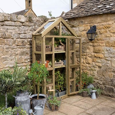 a wooden lean-to greenhouse in the corner of a patio