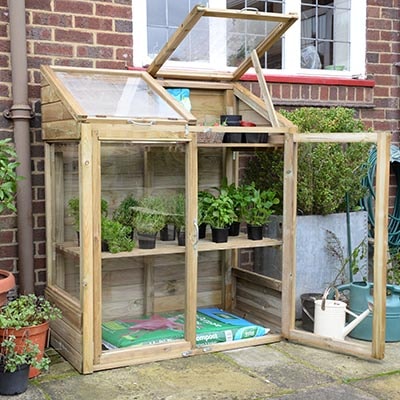 a mini wooden greenhouse containing plants and a bag of compost
