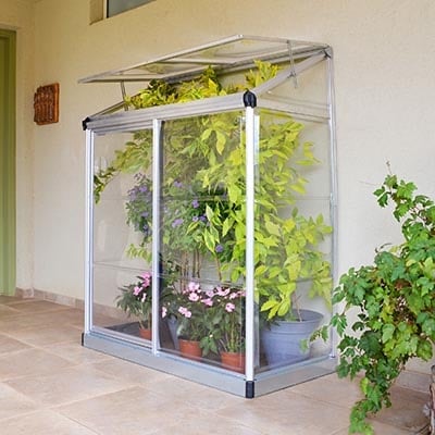 a silver-framed lean-to greenhouse full of plants