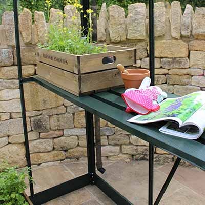 A seed tray and gardening tools sat on green greenhouse staging