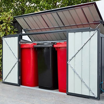 The 7x3 Lotus Grey Metal Triple Bin Store, situated on a patio, with doors open and 3 wheelie bins inside.