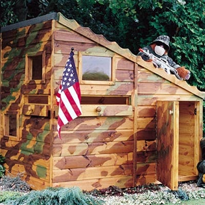 a wooden playhouse, painted in camouflage colours, with 2 windows, an open door and displaying an American flag