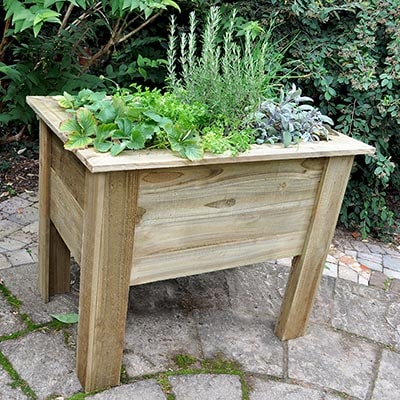 a deep wooden planter with 4 legs, containing a range of plants