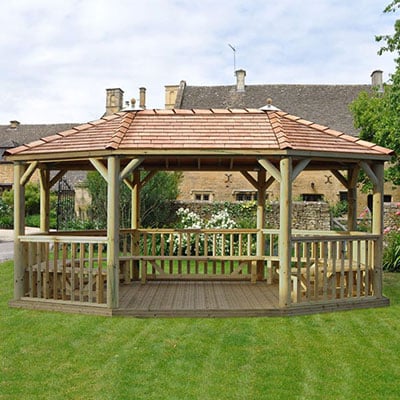 A large, oval, furnished wooden gazebo with a cedar roof