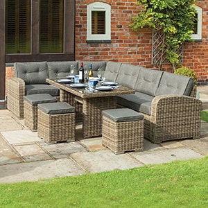 A grey rattan garden table and chairs corner dining set, table laid, situated on a patio.