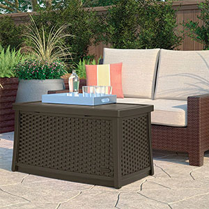 A drinks tray resting on top of the Suncast Elements Plastic Garden Coffee Table (with Storage), which is situated on a patio, next to a garden sofa.